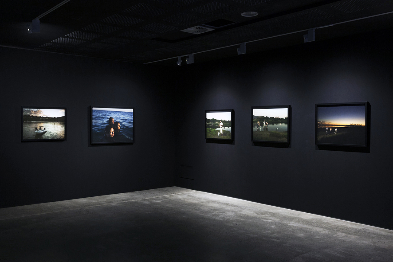 ​​​​​​​Installation view of five photographs mounted onto a black wall. 