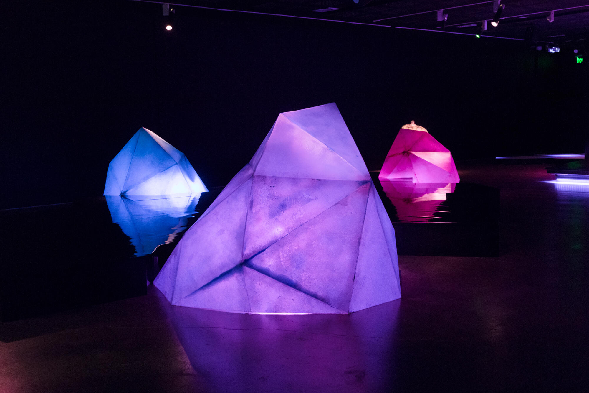Installation view of three geometric shapes. The colours of each shape is blue, purple and pink.