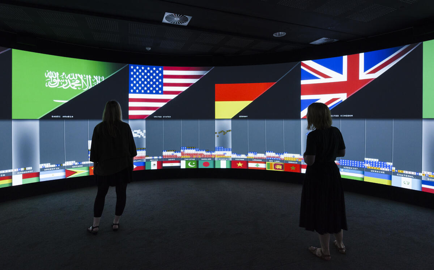 ​​​​​​​Two people looking at a screen showing flags from different countries.