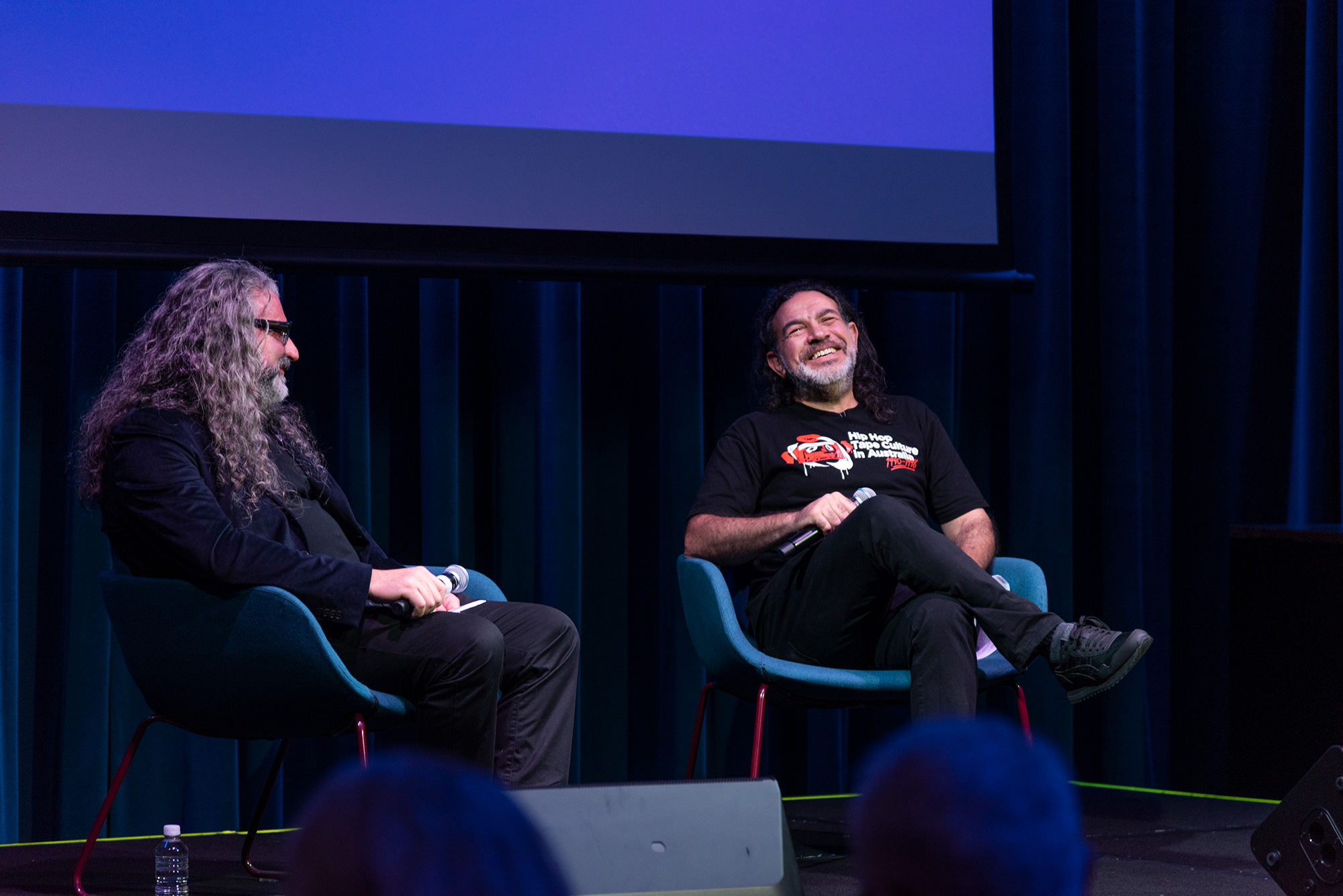Michael Dagostino and Khaled Sabsabi sit on stage, speaking together during a public discussion.