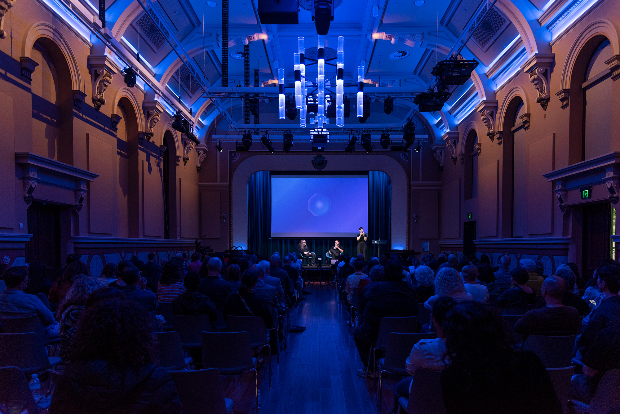 Michael Dagostino and Khaled Sabsabi sit on stage in conversation in front of a large audience.