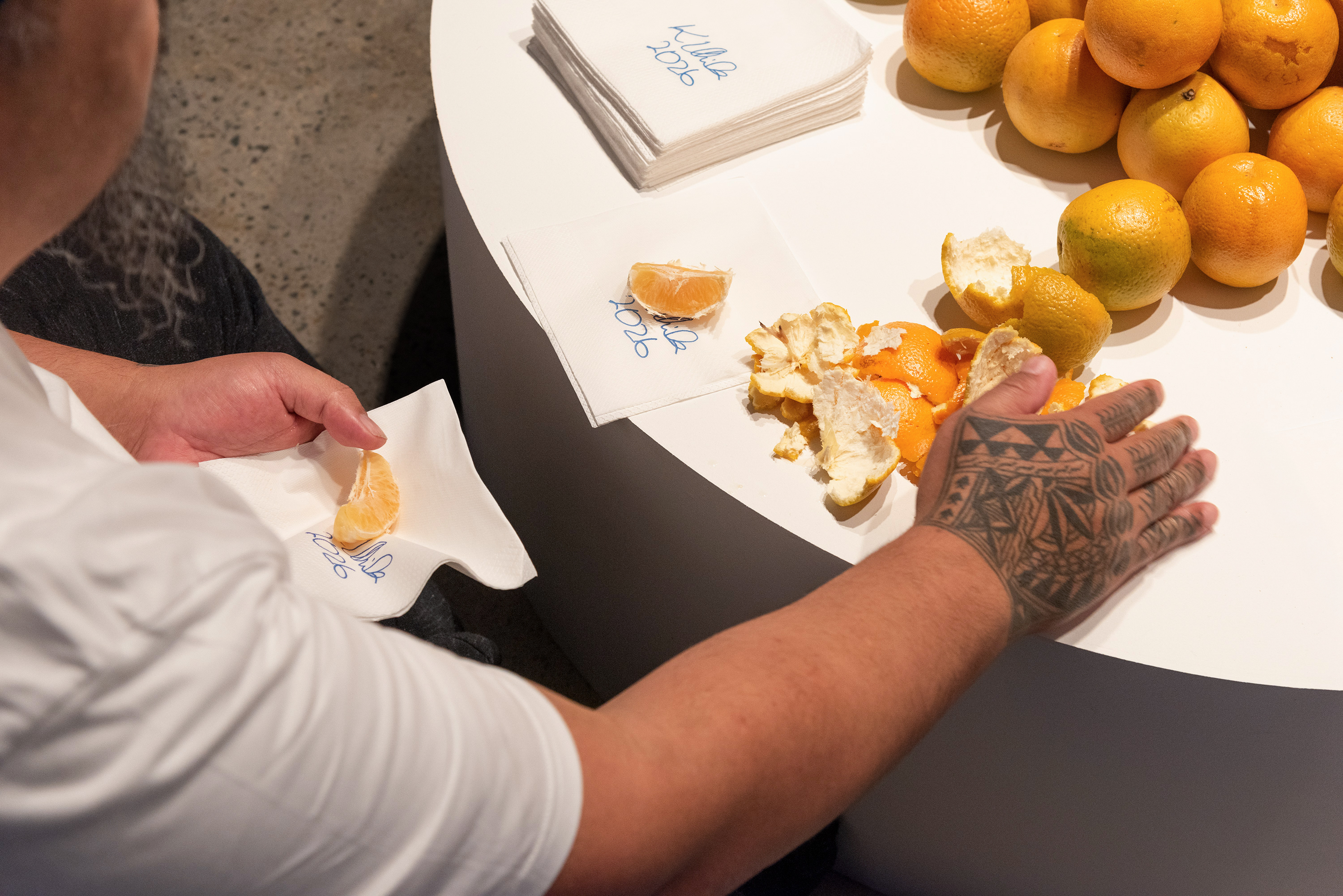Tattooed hand on a round plinth with peeled oranges and napkins.