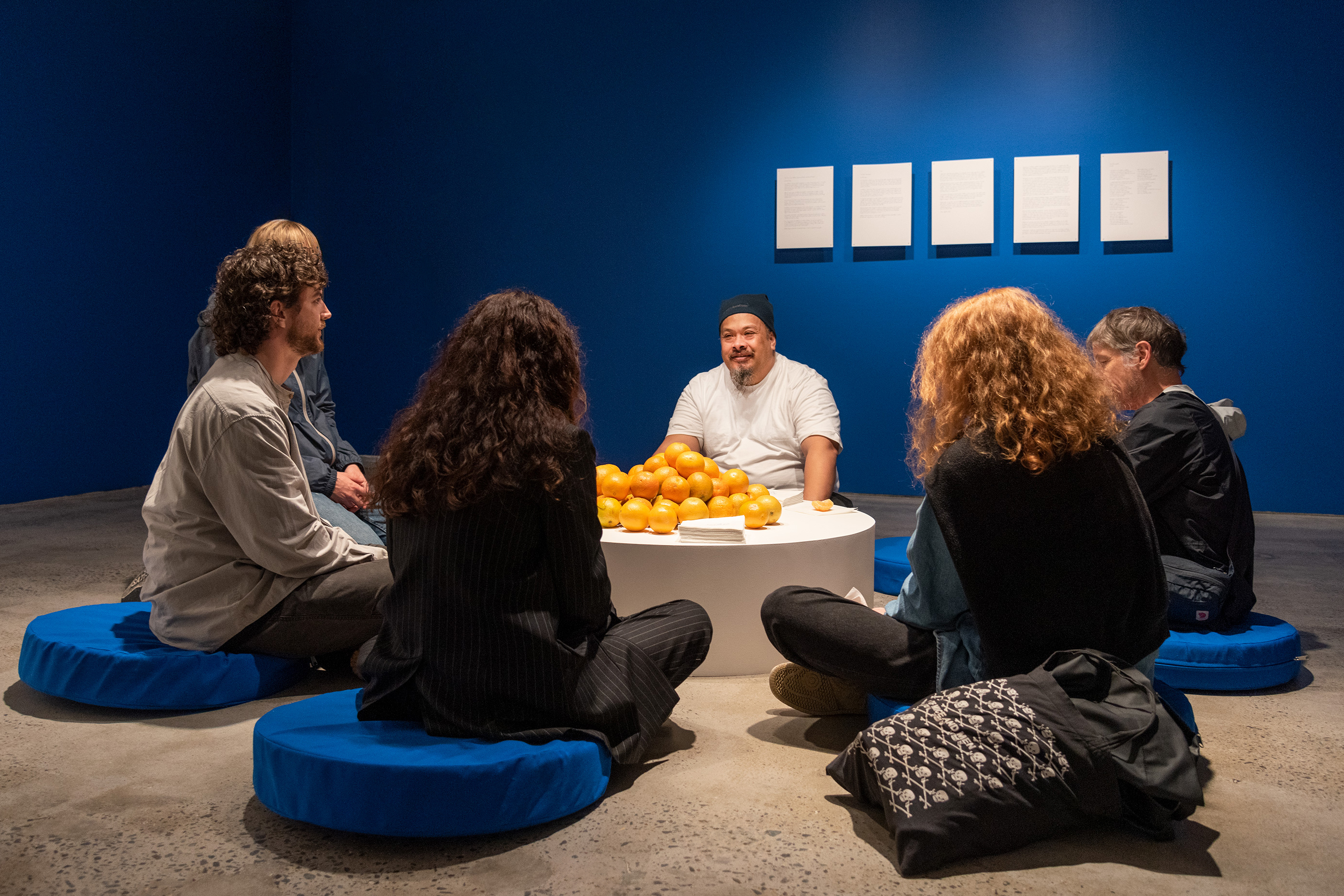 Kalisolaite ’Uhila with a pile of oranges and napkins, surrounded by five people.