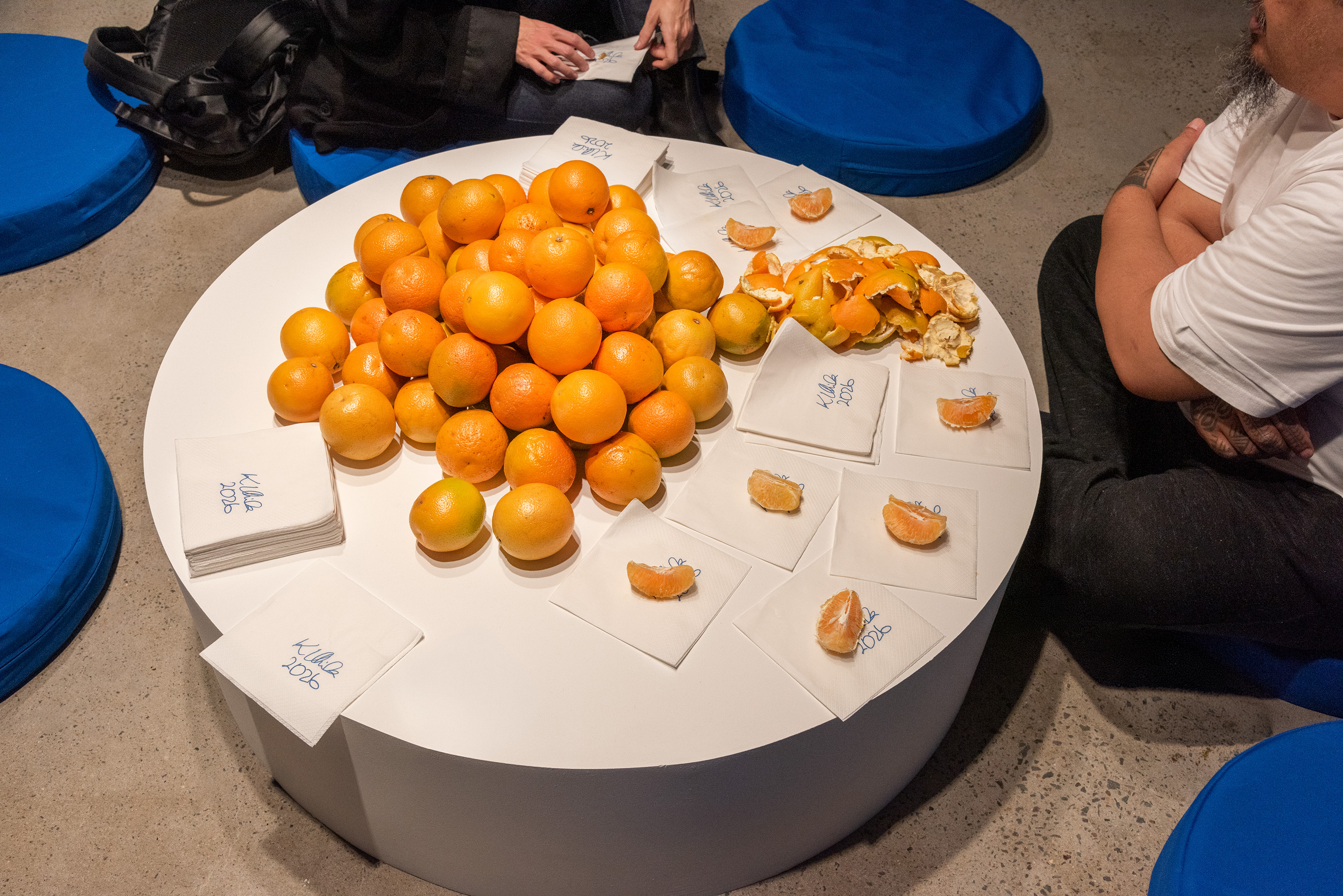 Peeled and unpeeled oranges with napkins on a white round plinth.