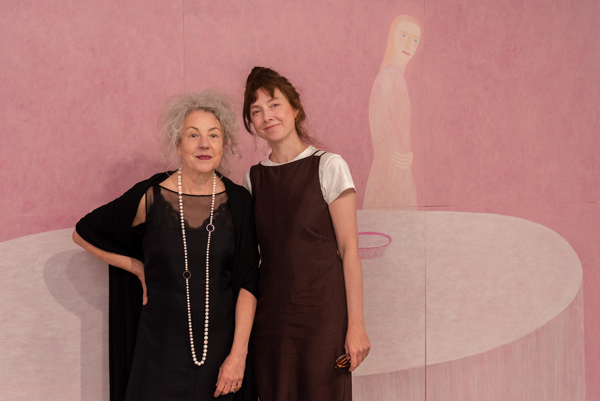 Artist, Heather B. Swann and Elspeth Pitt stand in front of a large pink painting depicting a pale figure beside a white circular table, posing within a gallery setting.
