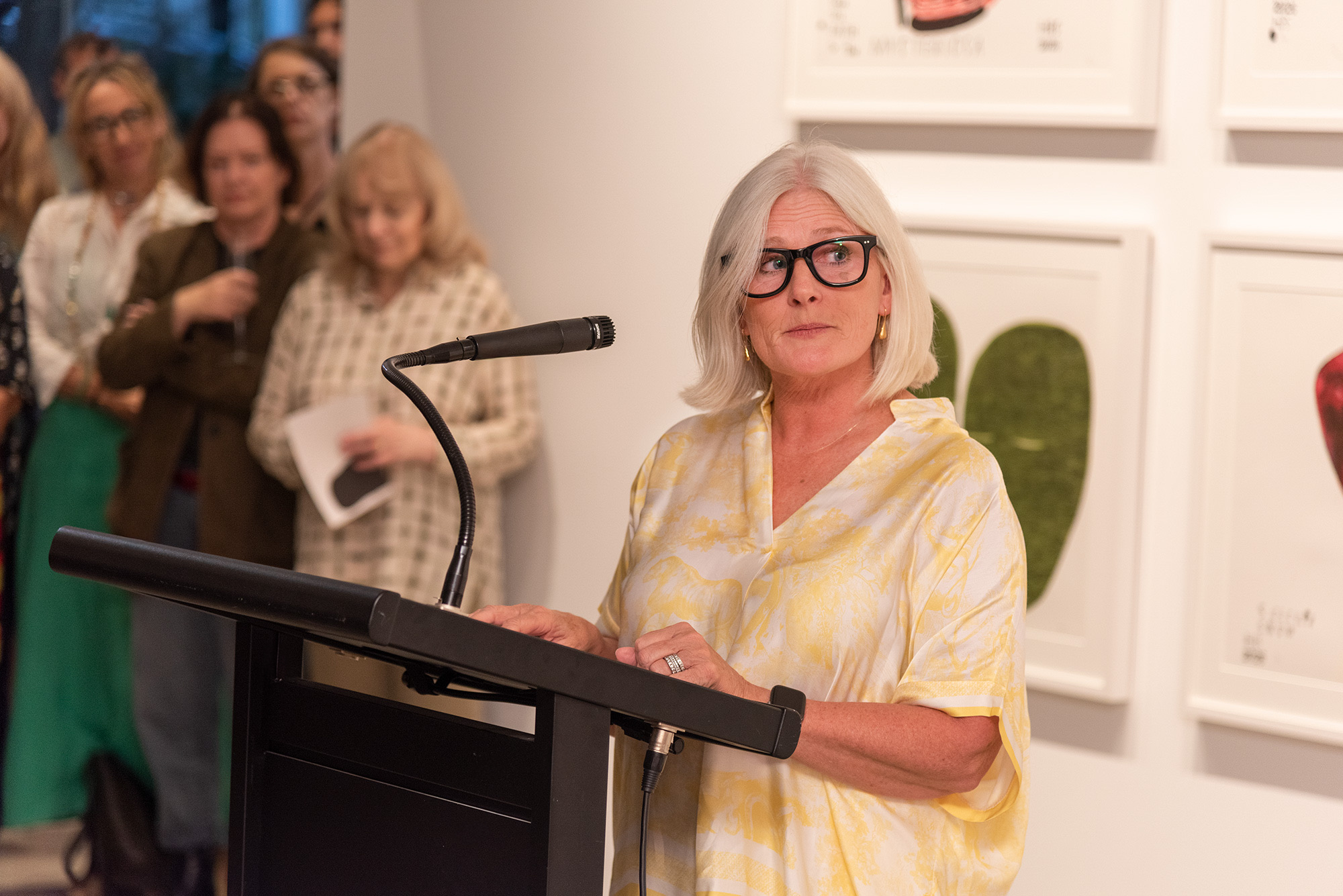 Copyright Agency's CEO Josephine Johnston stands at a lectern in front of a gallery audience, with framed artworks visible in the background.