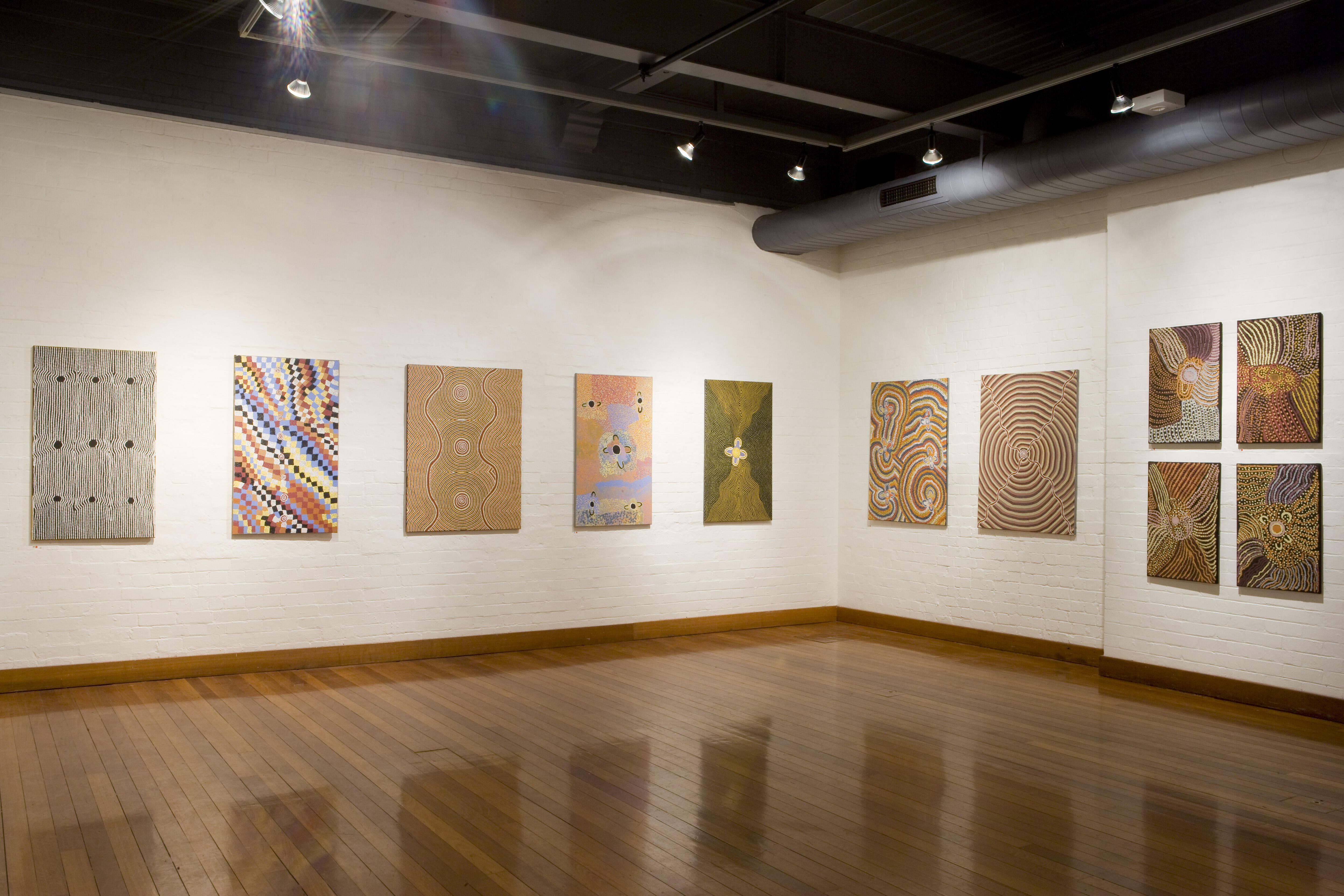 Installation featuring Papunya Tjupi Aboriginal art, with multiple contemporary Indigenous acrylic paintings arranged on white walls.