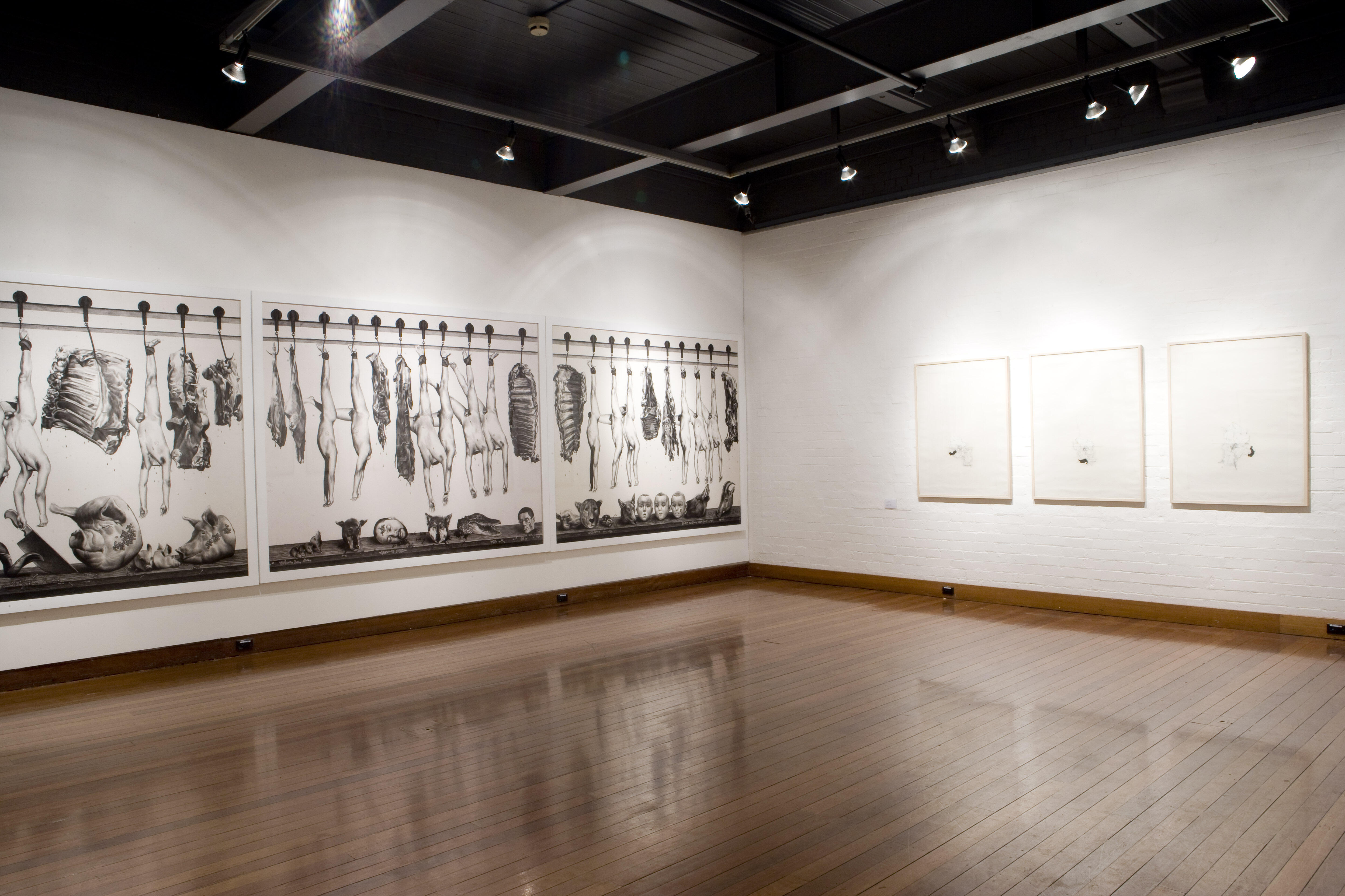 Installation view showing multiple large black-and-white graphite drawing.