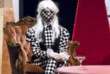 A figure of a person sitting on a chair dressed in black and white checkered clothing 