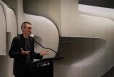 David Teh in a black outfit stands at a podium, gesturing while speaking.
