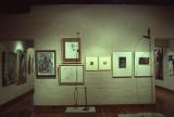 Gallery wall displaying framed abstract artworks alongside two tall, minimalist metal sculptures in a contemporary exhibition space.